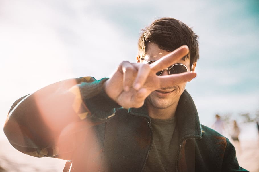 shallow focus photography of smiling man doing peace sign, man wearing black jacket