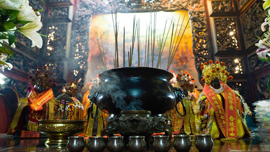 black cooking pot near flowers, long-angle photo of incense sticks struck on a black cauldron in front of a painting in a well-lit temple