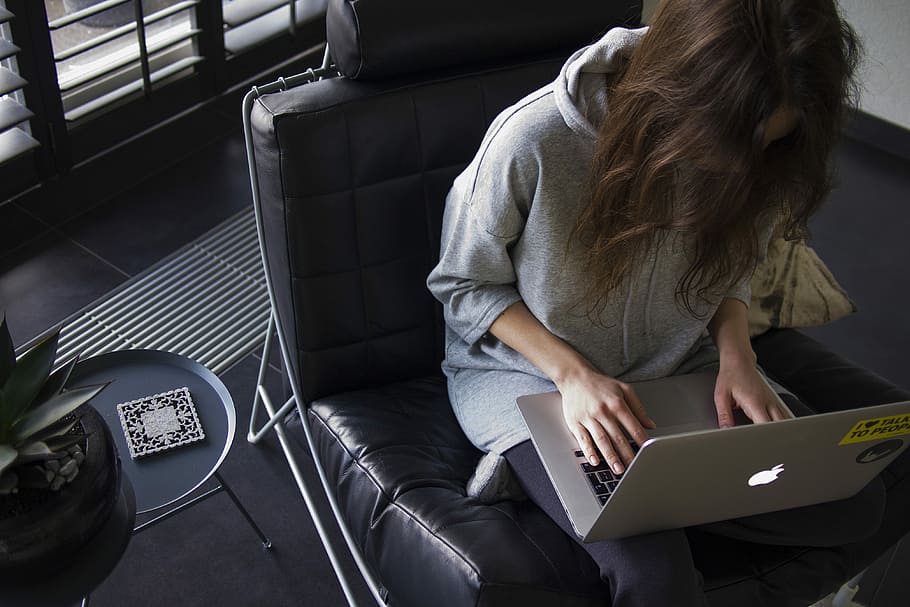 woman in blue chambray long-sleeved top sitting on black leather chair with silver MacBook on lap, woman in gray pullover hoodie using MacBook seating on black sofa chair, HD wallpaper