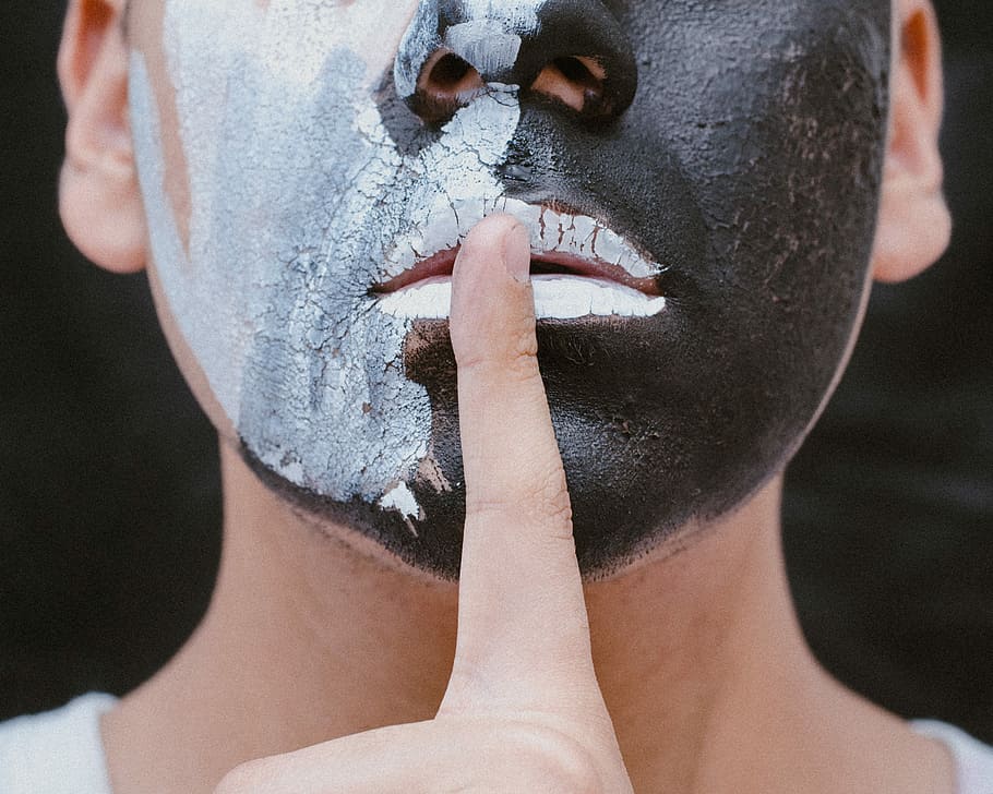 person with black and white face paint with finger on mouth doing the quiet gesture, man face with black and white face painting