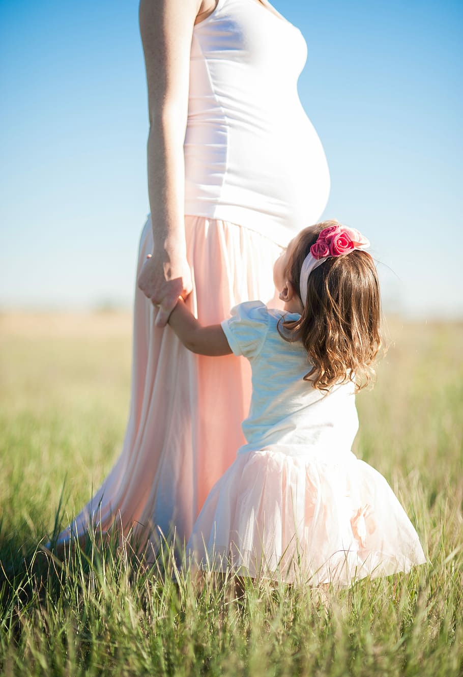girl in white and pink puff sleeve dress near pregnant mother standing on green grass during daytime HD wallpaper