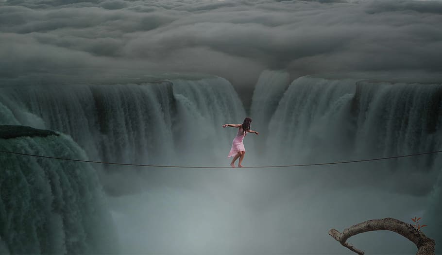 photograph of woman about to cross on rope above waterfalls, waters