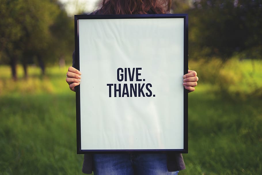person holding rectangular black wooden photo frame with Give. Thanks. print, white and black give thanks wall decor