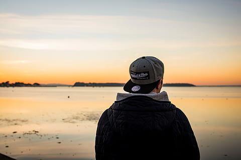 man wearing cap standing facing body of water, man wearing black jacket and gray flat-brim cap standing near body of water HD wallpaper