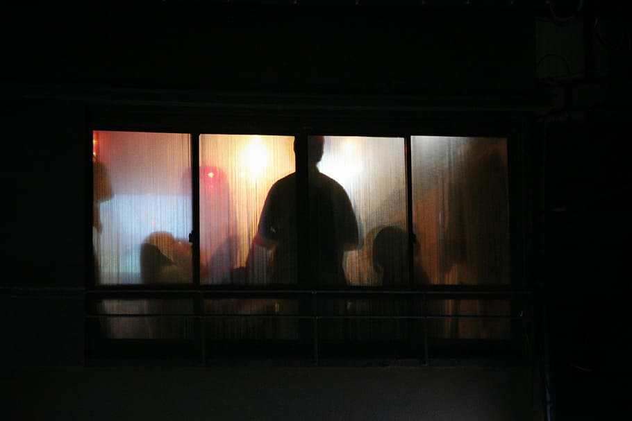 silhouette photo of man standing window pane, silhouette of group of people inside a room