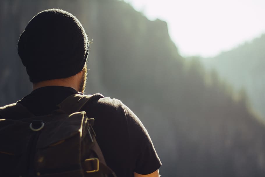 man wearing black t-shirt and knit cap fronting mountains, selective focus photo of man wearing black shirt and cap HD wallpaper