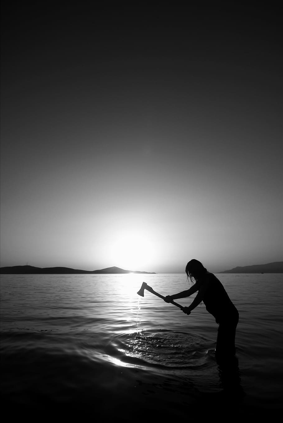 silhouette photo of person holding axe on body of water, black and white