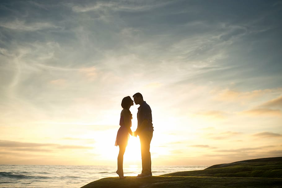 silhouette of man and woman facing each other near body of water