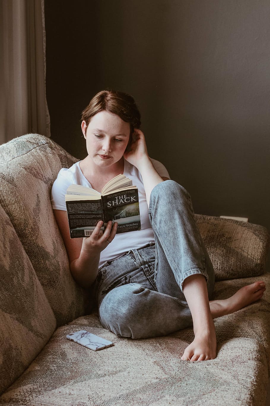 woman sitting on sofa while reading book inside room, woman sitting on gray couch while reading a book