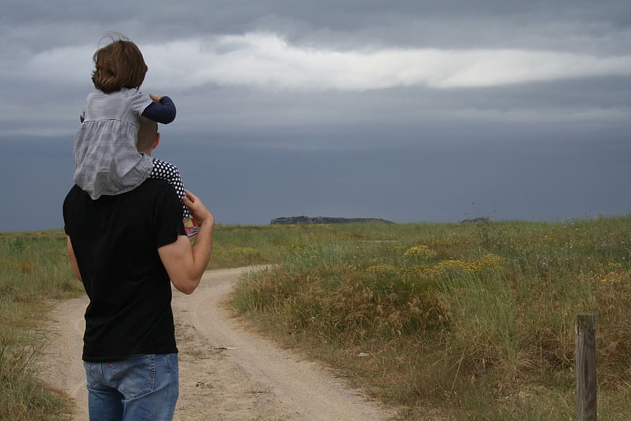 man in black shirt and blue jeans carrying children on green grass field during daytime HD wallpaper