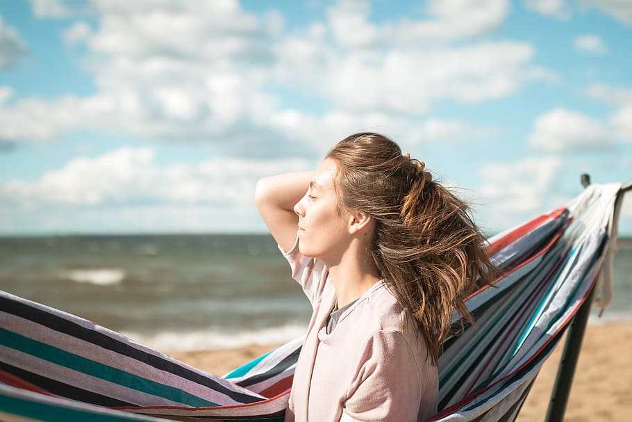 woman holding her hair backwards while sitting beside portable hammock on seashore during daytime, woman beside to hammock with stand HD wallpaper