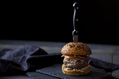 burger skewered with knife near black textile, burger with slice of tomato and lettuce with kitchen knife HD wallpaper