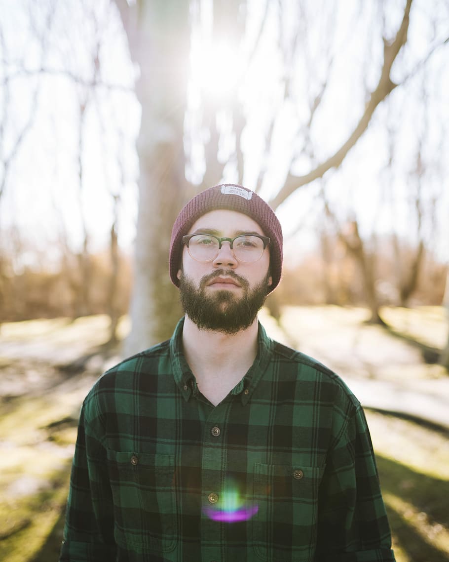 shallow focus photography of man standing near trees, man wearing eyeglasses in front of brown tree during daytime HD wallpaper
