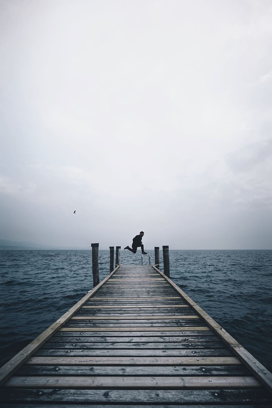 man jumping on brown wooden dock in middle of body of water, person in black pants jumping over brown wooden dock HD wallpaper