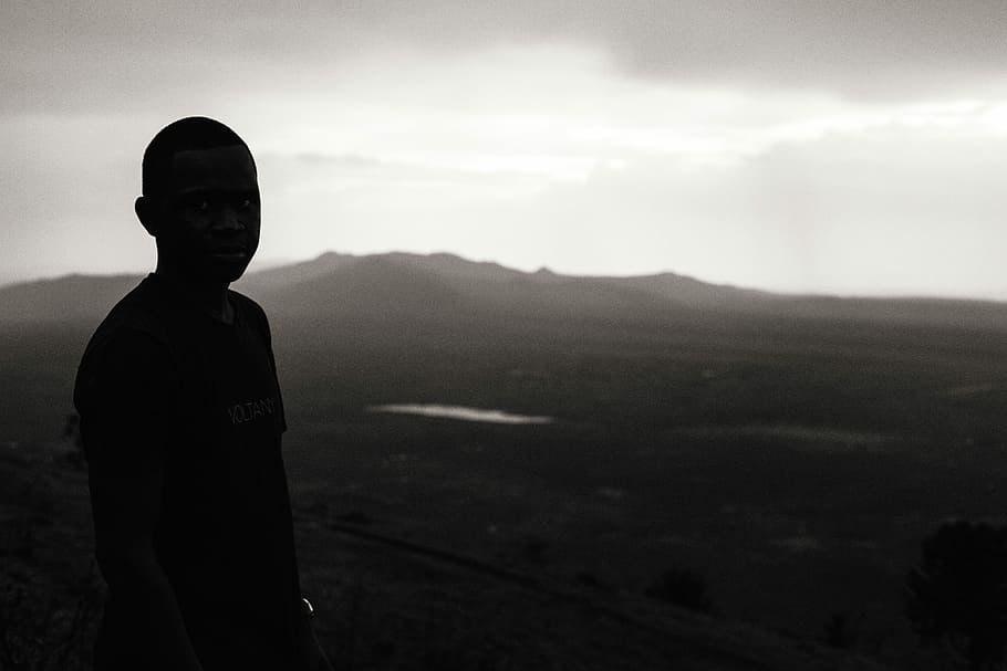 boy standing on bare hill during foggy day, silhouette photo of boy looking mountain during daytime HD wallpaper