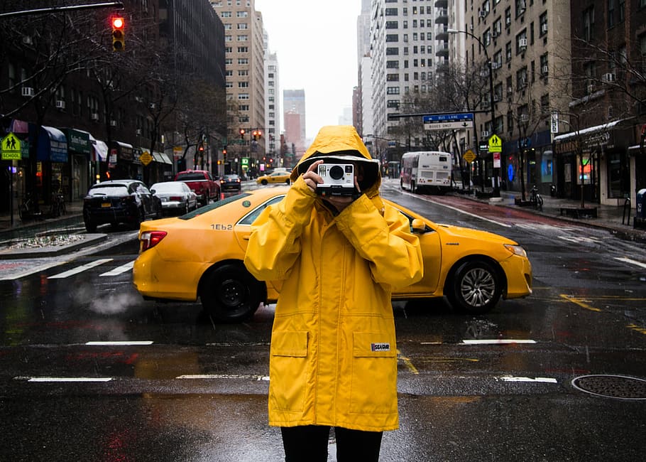 man standing on road while holding camera, person with raincoat taking photo in the middle of the street