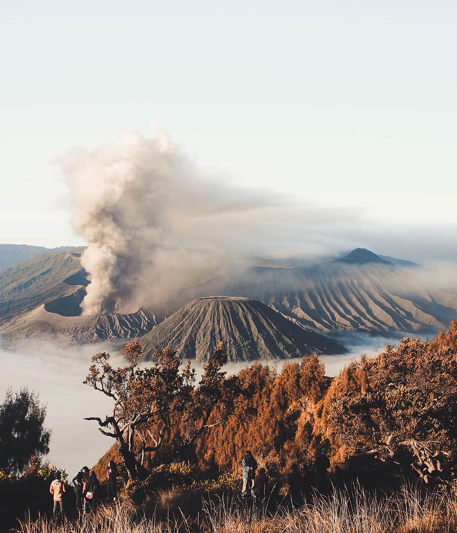 person standing on cliff with volcano background, erupting volcano surrounded by clouds HD wallpaper