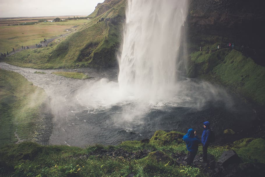 two person wearing blue hoodie standing on ground in front of waterfalls, times lapse photography of waterfalls HD wallpaper