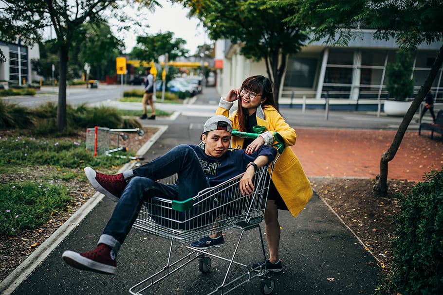 man sitting in shopping cart during daytime, man riding grey shopping cart in front of woman, HD wallpaper
