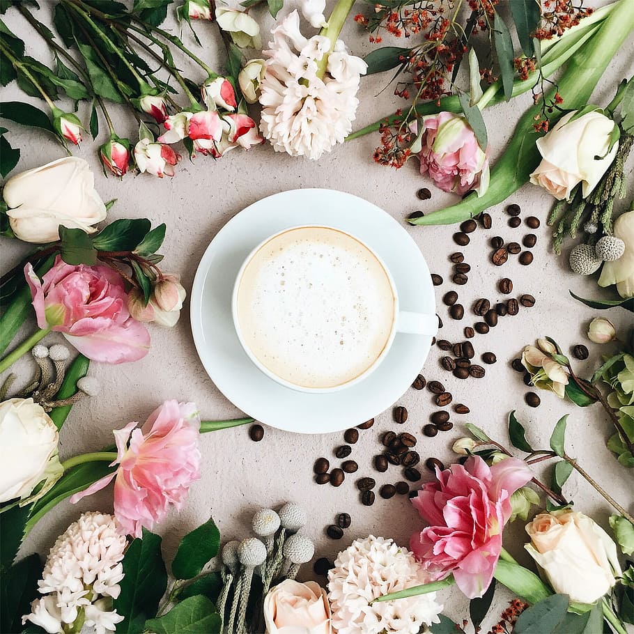 cappuccino filled white ceramic coffee cup on white ceramic saucer surrounded by assorted-type of flowers and coffee beans, cup filled with coffee on top of saucer surrounded by flowers HD wallpaper