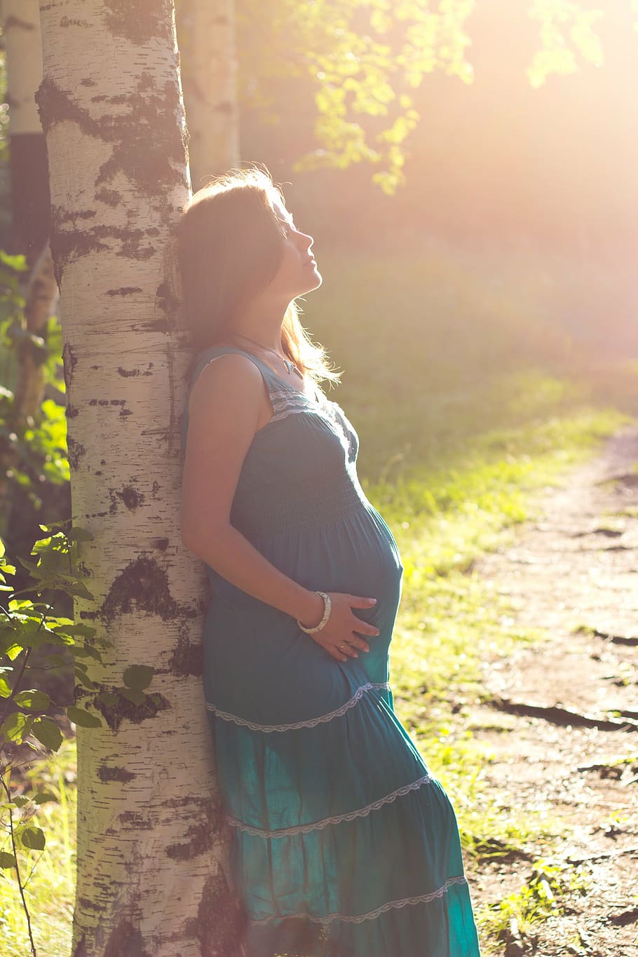 pregnant woman wearing blue maxi dress leaning on tree, pregnancy