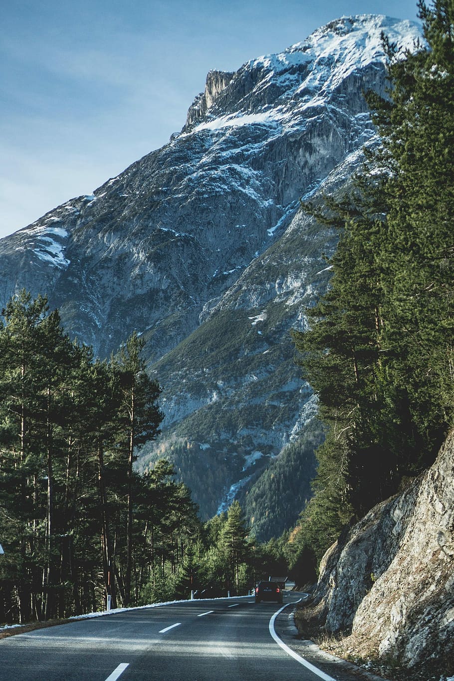 photograph of concrete road between trees and cliff with mountain background, gray asphalt road HD wallpaper