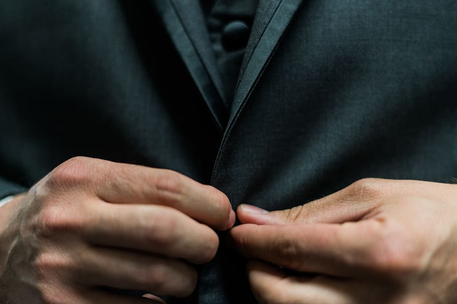 person holding black suit jacket button, man holding on clothes button