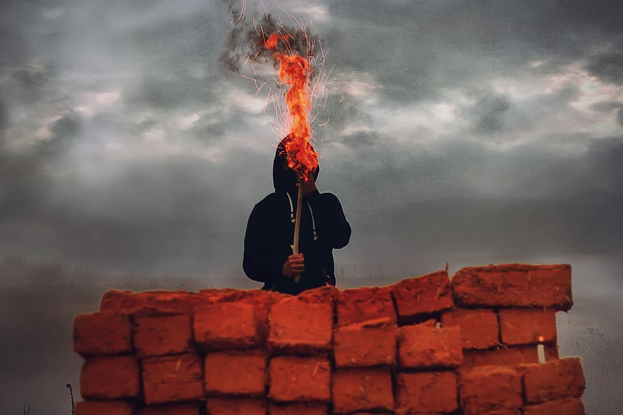 man holding torch light standing on red concrete rooftop, person holding torch under gray clouds during daytime HD wallpaper