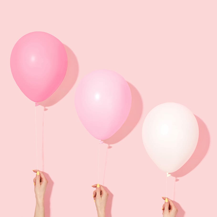 person holding pink and white balloon, three pink and white balloons