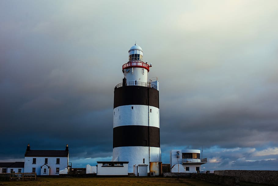 white and brown mainden's tower under cloudy sky, white and black lighthouse near white buildings under grey clouds HD wallpaper
