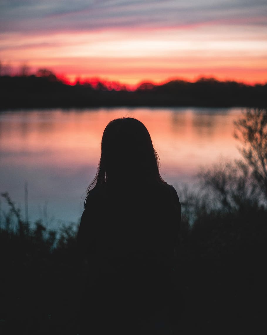 woman facing on body of water during sunset, silhouette of woman
