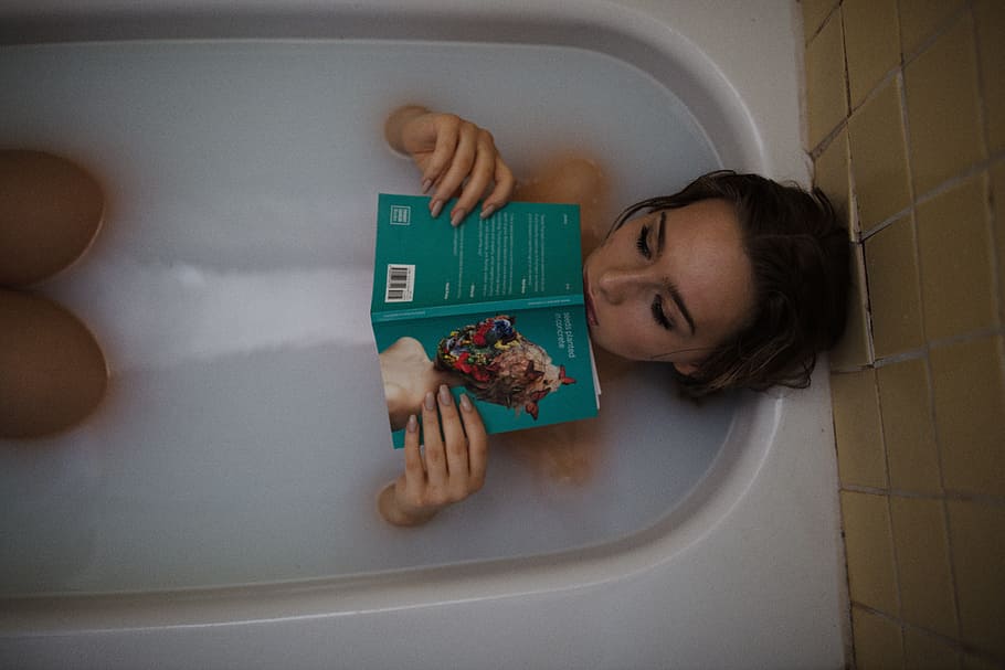 woman holding green covered book on white ceramic bathtub, people