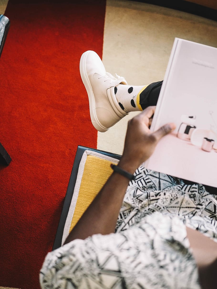 person holding book sitting on orange chair, person wearing white sneaker reading book while sitting HD wallpaper