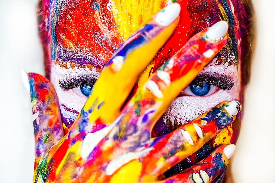 red, yellow, and blue floral textile, person filled with body painting with her hand on her face
