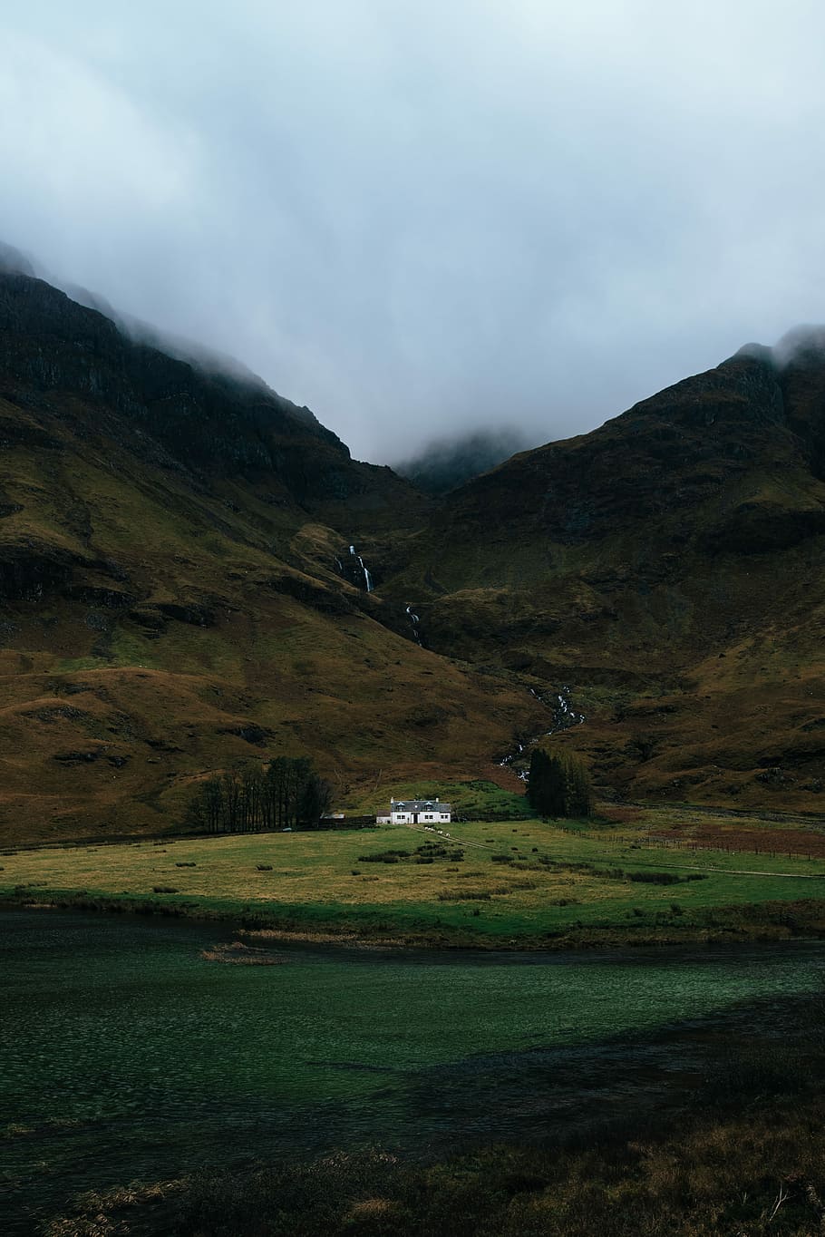 white and gray painted house below brown mountain taken at cloudy morning, white house alone on grass field near mountain range HD wallpaper
