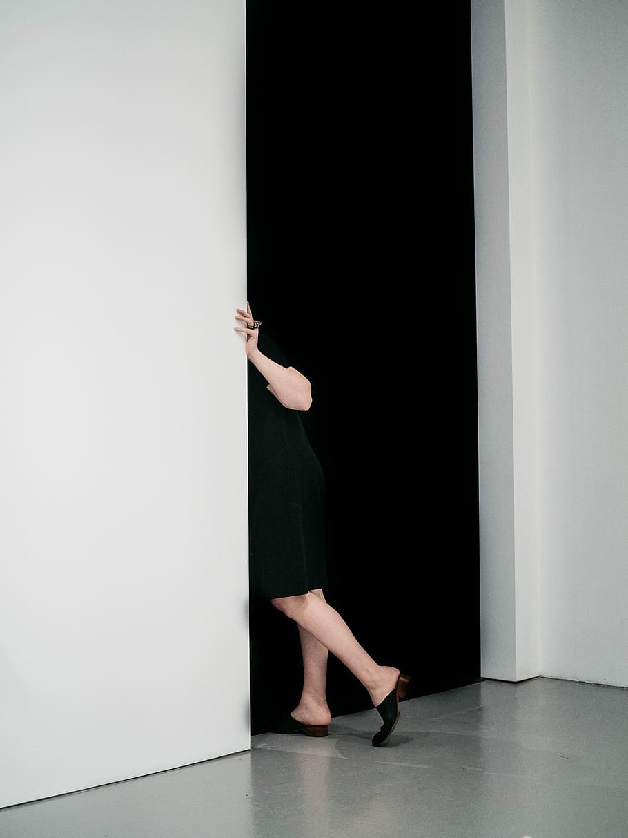 woman standing sneaking on door inside white painted room, woman in black dress peaking beside white wall HD wallpaper