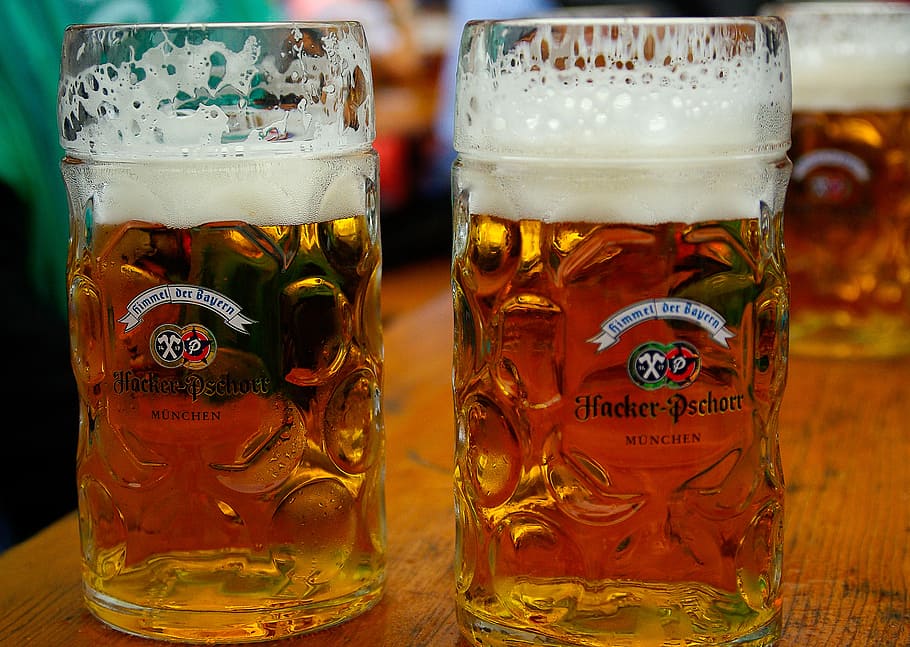 two beer filled clear beer glass mugs on brown wood surface, munich