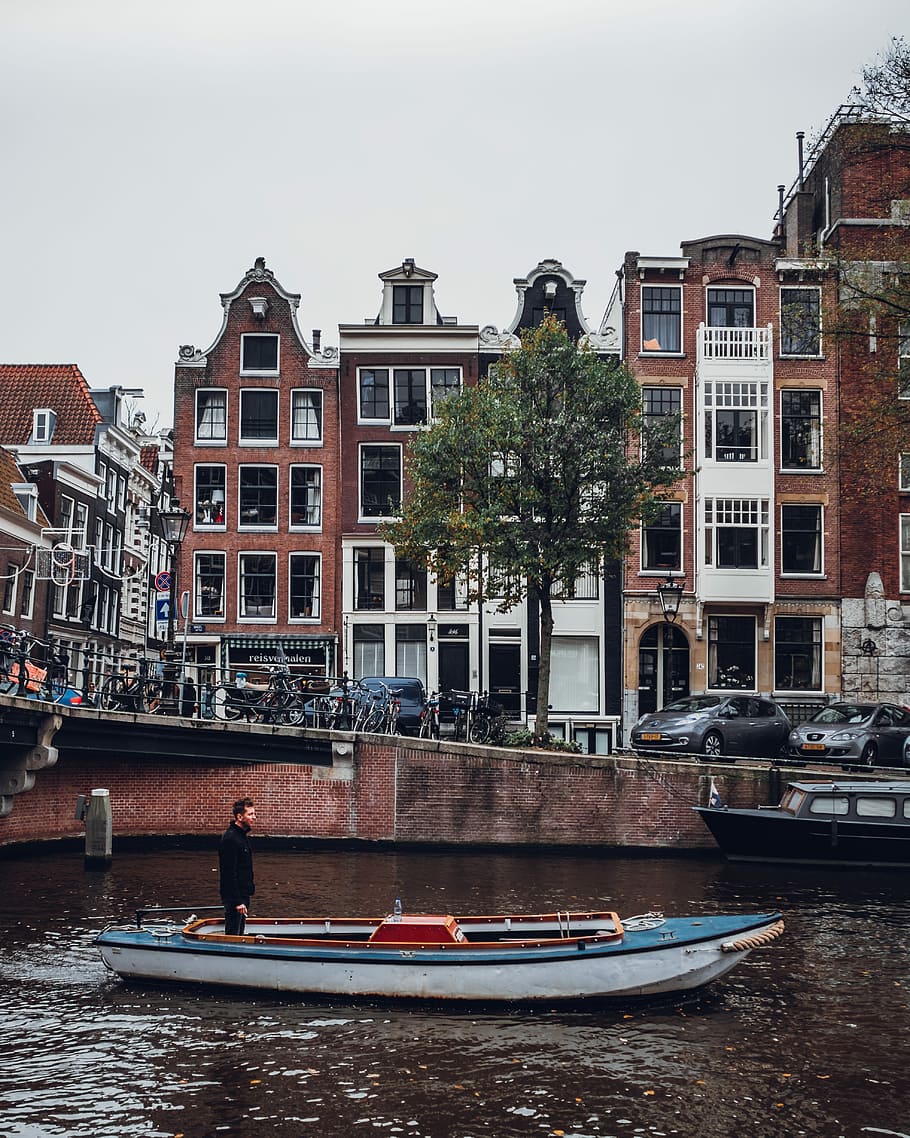 brown and white concrete building during daytime, man standing on motorboat near building HD wallpaper