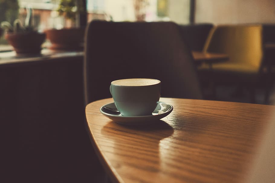 shallow focus photography of teacup with saucer on top of wooden table, blue ceramic coffee cup on table near chair