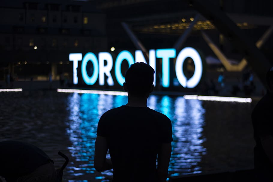 man facing Toronto LED signage, silhouette photo of man standing in front of fountain with Toronto neon freestanding sign HD wallpaper