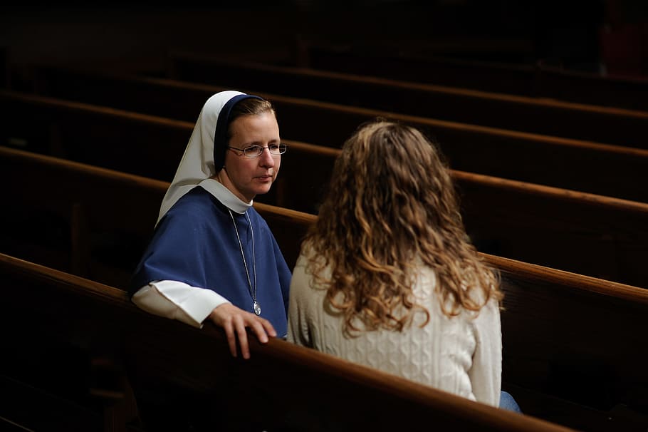 photo of woman in white long-sleeved shirt talking to a nun, woman wearing white shirt sitting beside nun in church