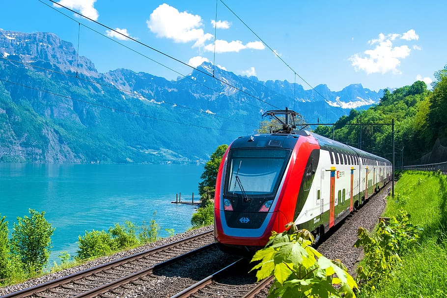 white, black, and red train on rail near body of water, passenger train