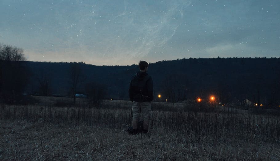 man wearing black jacket standing near grass looking at mountain, man standing near mountain during starry night HD wallpaper