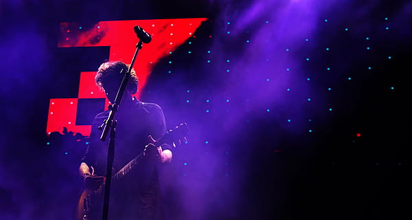 man playing guitar standing in front of microphone with stand HD wallpaper