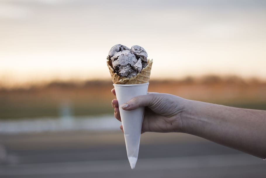 person holding ice cream, person holding cone of ice cream, rocky road ice cream