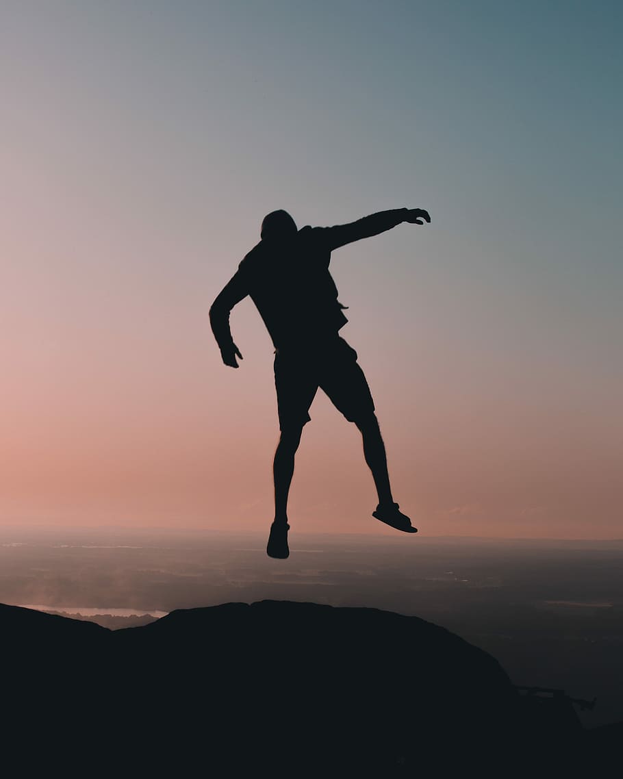 silhouette of man jumping on cliff at golden hour, man jumping on mountain