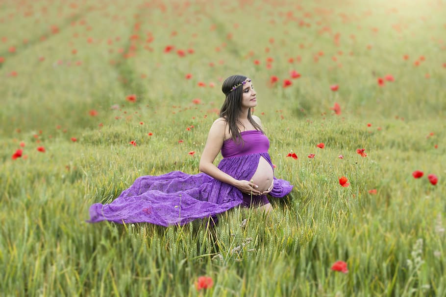 pregnant woman in purple dress in the middle of grass field, pregnancy