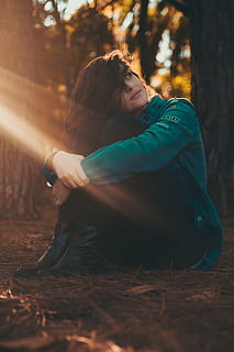 Selective Focus Photography of Woman in Green Jacket and Black Pants Sitting on Field Surrounded With Trees HD wallpaper