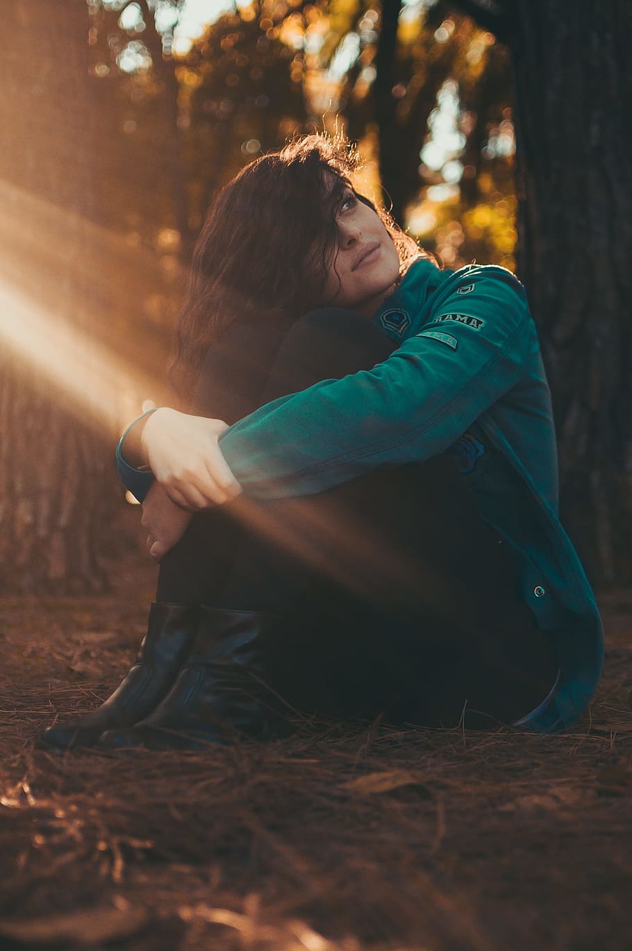 Selective Focus Photography of Woman in Green Jacket and Black Pants Sitting on Field Surrounded With Trees HD wallpaper