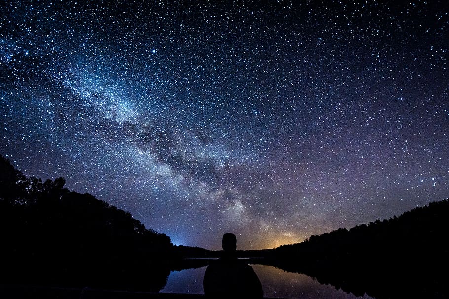 silhouette of person standing under starry sky, silhouette of person near body of water under starry night
